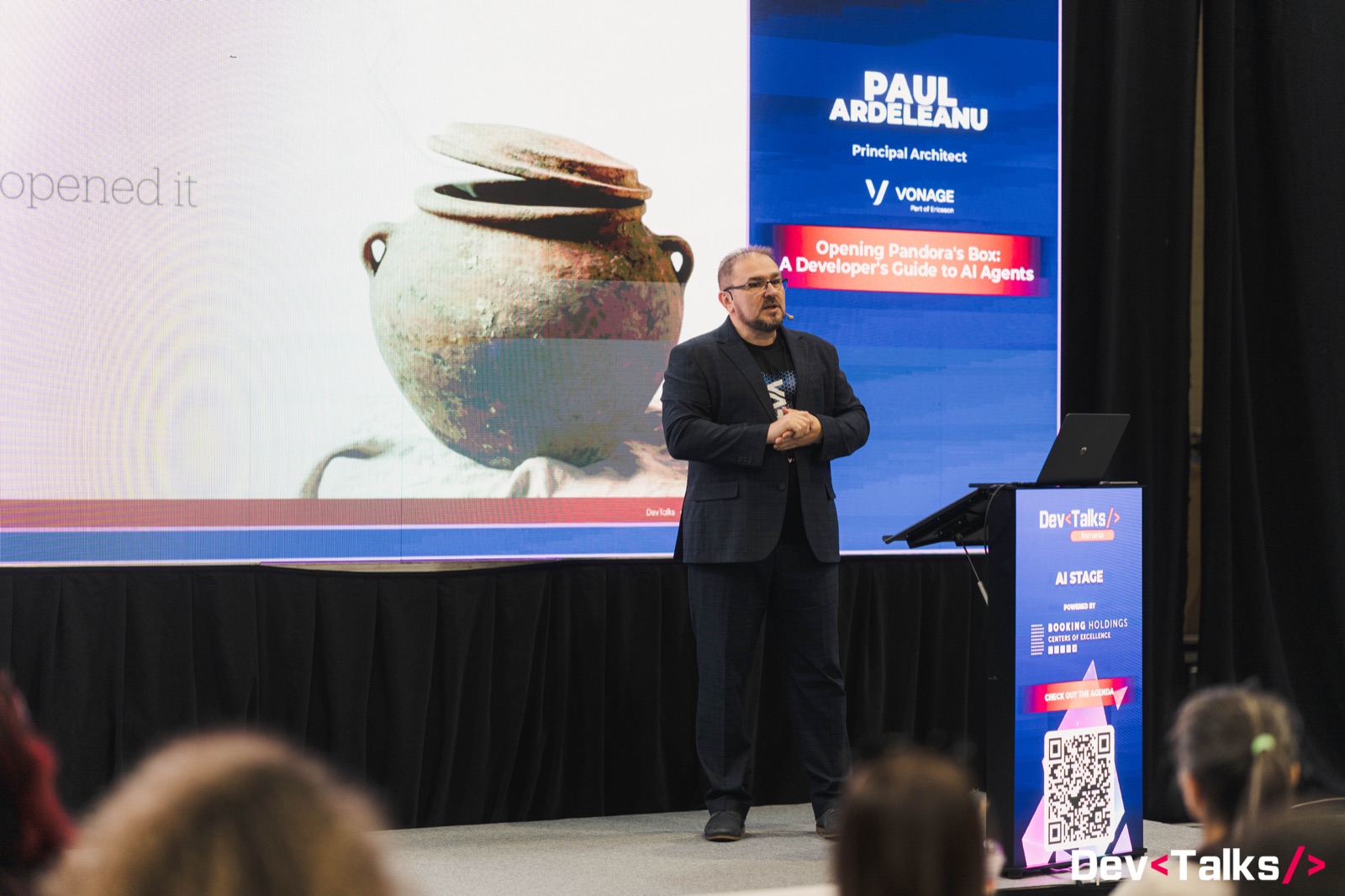 Paul Ardeleanu on the AI Stage at DevTalks Romania, mid-gesture, with the Opening Pandora's Box speaker banner behind him.